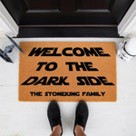 Personalized sci-fi themed welcome doormat with black text on natural coir fiber, featuring a space movie quote and family name customization for a front porch entry, shown on a white floor with a toy starfighter and helmet