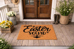 Easter Squad coir doormat featuring black script text and bunny nose whiskers on a natural fiber welcome mat, displayed on a rustic front porch with spring flowers and wood decor for a festive seasonal home entrance entryway