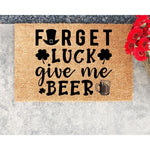 Funny St. Patrick's Day coir doormat featuring a leprechaun hat, shamrocks, and a beer mug graphic with the text Forget Luck Give Me Beer, perfect for a festive front porch welcome mat or a humorous home entryway decor piece.