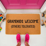 Grandkids Welcome doormat for grandparents, a funny coir welcome mat with black text placed on a porch with toys, perfect for a front door entrance to show off a humorous family personality and keep the home entryway stylish.