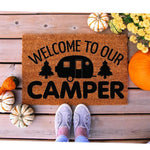 Welcome to our camper doormat featuring a travel trailer and pine tree design on natural coir fiber, perfect for outdoor camping decor, RV porch mats, or a fall seasonal entrance rug placed on a wood deck with pumpkins and