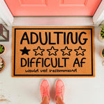 Funny Adulting Difficult AF doormat with a one-star review design, featuring a natural coir fiber welcome mat on a front porch, perfect for a sarcastic home decor entrance or a humorous housewarming gift for friends and family.