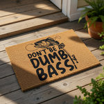 Funny fishing doormat with a bass fish graphic and the text Don't Be A Dumb Bass, featuring a natural coir fiber welcome mat design that is perfect for a fisherman porch decor or a humorous outdoor entrance rug for any fishing