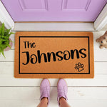 Personalized family name doormat with a paw print design, featuring a natural coir fiber texture on a white porch, making a stylish custom welcome mat for pet lovers and a durable outdoor floor rug for your front door entrance.
