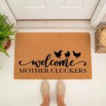 Funny chicken welcome doormat with Mother Cluckers text and black hen silhouettes on natural coir fiber, a humorous farmhouse style front porch rug for farm animal lovers and home decor enthusiasts placed at a white front door.