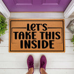 Let's Take This Inside coir doormat featuring bold black text on a natural fiber welcome mat, placed on a white porch in front of a purple door, perfect for a funny housewarming entry rug or a stylish front door decor floor mat.