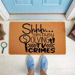 Funny crime show doormat for true crime fans, featuring a magnifying glass and footprint design on a natural coir welcome mat, perfect for a front porch entrance to show off your love for solving mysteries and watching TV crimes.