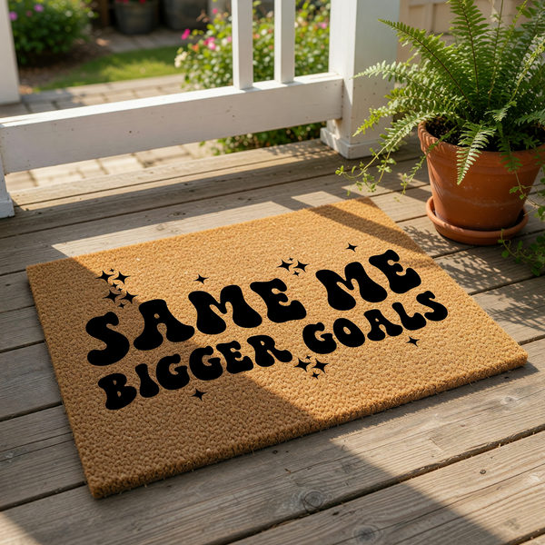 Same Me Bigger Goals doormat featuring bold retro typography on a natural coir welcome mat, placed on a front porch with a potted fern, perfect for a stylish entryway, housewarming decor, or a fun outdoor floor mat for your home.