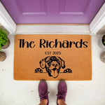 Personalized Labrador dog doormat with family name and established year, featuring a cute black lab illustration on a natural coir welcome mat placed at a purple front door for a custom housewarming or pet lover home entrance