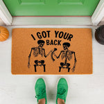 Skeleton I Got Your Back doormat for Halloween porch decor, featuring two black skeletons holding a spine on a natural coir welcome mat, perfect for a funny fall entryway rug or spooky home entrance floor mat for the holiday.