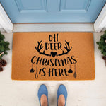 Oh Deer Christmas Is Here doormat featuring black text, antlers, and ornaments on a natural coir welcome mat, placed at a blue front door for a festive holiday porch decor look that adds seasonal cheer to your home entryway.