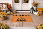 Personalized dog breed doormat featuring a cute shaggy puppy illustration on a natural coir welcome mat, displayed on a fall porch with pumpkins and flowers, perfect for a custom family name housewarming entrance decor piece.