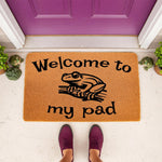 Frog welcome doormat with Welcome to my pad text, a funny coir outdoor rug for front porch decor featuring a cute frog illustration, perfect for animal lovers and housewarming entryways in front of a purple door with small frog