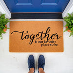 Together is our favorite place to be doormat, a natural coir fiber welcome mat with black script lettering placed on a front porch, making a stylish housewarming decor piece for your entryway or front door step for new homeowners.