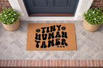 Tiny Human Tamer doormat featuring bold retro typography on a natural coir fiber welcome mat, perfect for a front porch entry.