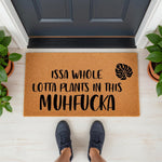 Funny plant lover doormat with a monstera leaf design and bold text reading Issa Whole Lotta Plants In This Muhfucka, placed on a porch floor with potted plants and a person standing on the natural coir fiber welcome mat entry