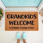 Grandkids Welcome doormat for grandparents, a funny coir welcome mat with black text on a natural fiber rug, placed on a porch in front of a light blue door with a person wearing light blue shoes standing on the front entry floor