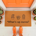 Cactus welcome doormat with funny plant pun text What is up succa, featuring a natural coir fiber rug design with potted succulent illustrations for a front porch entry, perfect for housewarming decor or a stylish home entrance.