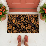 Floral pattern doormat with a black and natural tan design, featuring a stylish botanical print on this durable welcome mat for a front porch entrance, shown on a white floor with potted orange flowers and a person wearing casual