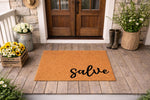 Natural fiber coir doormat with the word salve printed in black script, displayed on a rustic wood porch as a stylish front door welcome mat for home entryways, featuring a durable outdoor floor rug design for house decor.