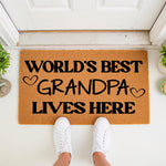 World's Best Grandpa doormat featuring bold black text and heart icons on a natural coir fiber mat, placed at a front door entrance as a decorative welcome mat for a grandfather's home, perfect for a housewarming or birthday
