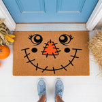 Scarecrow face doormat for fall porch decor, featuring a cute stitched smile and orange nose on natural coir fiber.