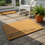 Funny coir doormat for front porch featuring the text I hope you brought wine, plants, and dog treats, this natural fiber welcome mat is a durable outdoor floor rug for pet lovers and plant enthusiasts on a rustic wood deck.