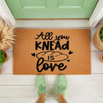All You Knead Is Love doormat featuring a bread loaf graphic on natural coir fiber, this funny kitchen welcome mat is a cute housewarming gift for bakers and home cooks placed on a front porch with green sneakers in the