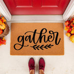 Gather fall doormat with black script text and leaf design on a natural coir welcome mat, displayed on a front porch with autumn pumpkins and leaves for seasonal home decor, perfect for a cozy farmhouse entryway or housewarming