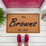 Personalized family name coir doormat featuring a custom established date, this durable natural fiber welcome mat is a stylish front porch decor piece for new homeowners or housewarming celebrations on a white wood floor.
