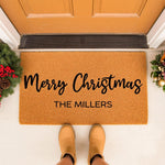 Personalized Merry Christmas doormat with family name, featuring a natural coir welcome mat for front porch decor, holiday entryway floor rug, and festive winter home entrance mat with seasonal greenery and pinecones on a porch.