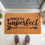 Perfectly Imperfect coir doormat for front porch entry, featuring a natural fiber welcome mat with black text and an arrow design, placed on a white floor in front of a gray door for a stylish and modern home entryway decor look.