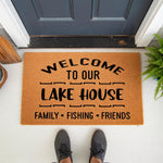 Lake House Welcome Doormat with natural coir fiber texture, featuring black text that reads Welcome To Our Lake House Family Fishing Friends, perfect for a rustic cabin porch decor or a personalized outdoor entrance floor mat.