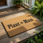Plant Mom coir doormat for front porch, featuring bold black text and a flower icon on natural fiber.