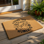 Funny Halloween doormat featuring a cute ghost holding a bone with the text I Found This Humerus, this natural coir welcome mat is a spooky porch decor essential for fall home entryways and seasonal outdoor front door decorations.