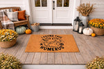 Funny ghost Halloween doormat with a skeleton bone design and I Found This Humerus text, featuring a natural coir fiber welcome mat on a porch decorated with pumpkins and fall flowers for a spooky seasonal home entrance decor