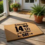 Funny Valentine's Day doormat with black text reading February 14th just another day on a natural coir fiber welcome mat, displayed on a front porch with potted plants for a humorous holiday home decor entrance design.