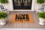 Love More Worry Less coir doormat featuring bold black typography on a natural fiber welcome mat, displayed on a front porch with rocking chairs and ferns to create a stylish entryway decor look for your home or housewarming gift.