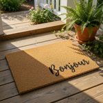 Bonjour welcome doormat featuring natural coir fiber texture on a wood porch, this stylish outdoor entry rug with black script lettering adds a charming touch to your front door decor and home entryway floor mat collection.