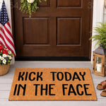 Funny Kick Today In The Face doormat featuring bold black text on a natural coir fiber welcome mat, displayed on a front porch with a dark wood door, American flag, and lantern for a stylish and motivational home entryway decor