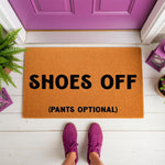 Funny Shoes Off Pants Optional doormat for front porch decor, featuring bold black text on a natural coir fiber welcome mat, placed on a white floor in front of a purple door for a humorous home entryway and housewarming gift