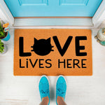 Cat lover welcome doormat with Love Lives Here text and a cat face silhouette design, featuring a natural fiber texture on a front porch setting with bright blue shoes standing in front of the entrance mat for pet owners.