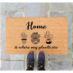 Plant lover welcome doormat featuring a natural coir fiber texture with black text reading Home is where my plants are and three potted houseplant illustrations, perfect for a front porch entry or a housewarming gift for