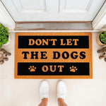 Funny dog lover doormat with the text Don't Let The Dogs Out, a natural coir fiber welcome mat for front porch entryways, featuring paw print designs and a bold black and orange color scheme for pet owners and home decor