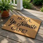 Funny Spanish coffee doormat for front porch, featuring a natural coir welcome mat with black text that reads Hola Ya Tomaste Cafe, a perfect housewarming gift for coffee lovers placed on a rustic wood deck with a potted fern