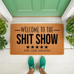 Funny welcome doormat with the text Welcome to the Shit Show and five stars, featuring a natural coir fiber texture on a front porch.