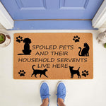 Spoiled Pets and Their Household Servants Live Here doormat, a funny coir welcome mat for cat and dog lovers featuring animal silhouettes and paw prints, placed on a porch in front of a blue door for a humorous home entryway