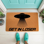 UFO welcome doormat featuring a black flying saucer graphic and the text Get In Loser, this funny outdoor floor mat is made of natural coir fiber and sits on a porch in front of a bright teal door for a quirky home entrance decor