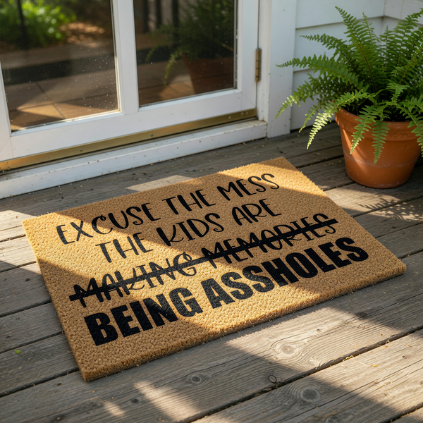 Funny doormat with rude text that says Excuse the mess the kids are making memories being assholes, featuring a natural coir fiber welcome mat design that is perfect for a humorous front porch entry or a sarcastic housewarming