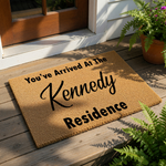 Personalized family name doormat featuring a natural coir fiber texture with black text that reads You've Arrived At The Residence, making this custom outdoor welcome mat a stylish housewarming decor piece for your front porch